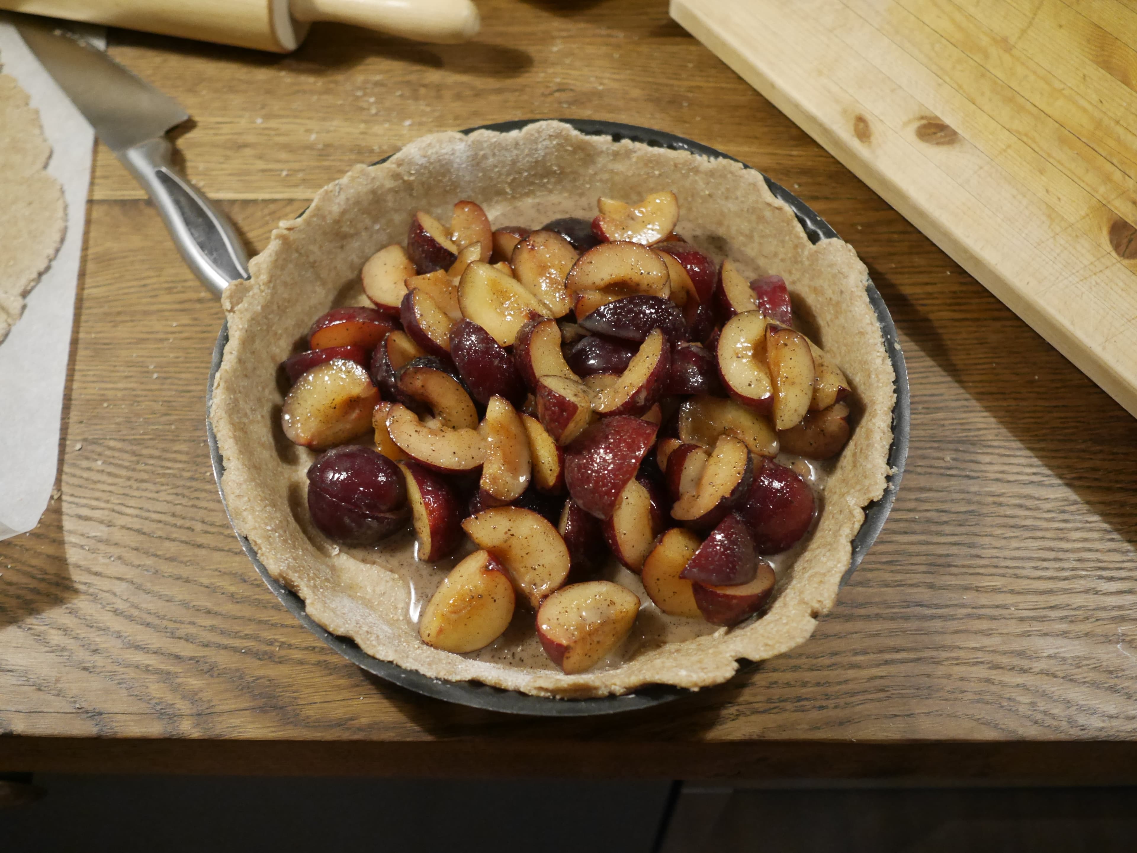 A pie dish with uncooked plum filling inside and no top pie crust.