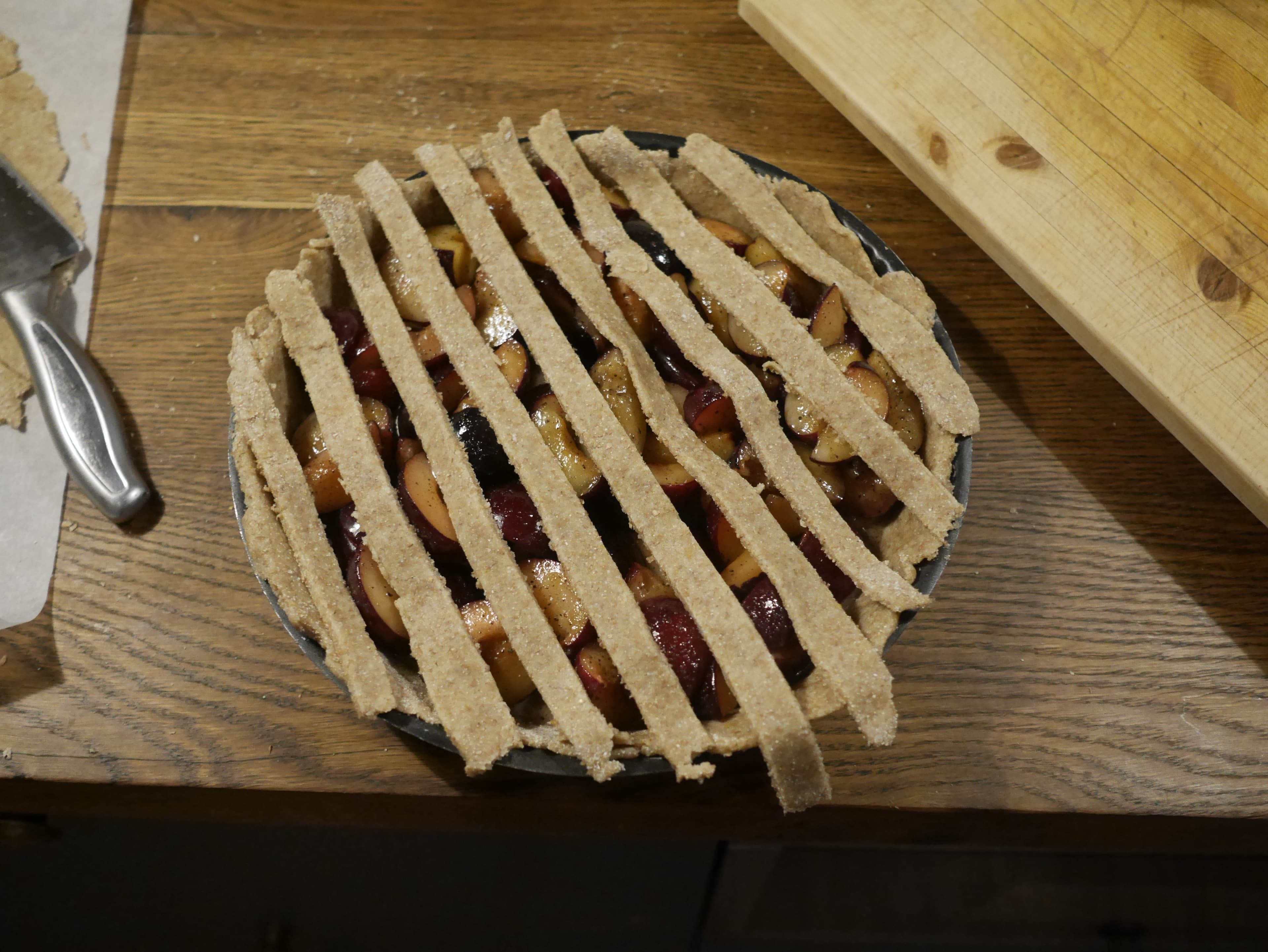 A dough lattice being placed on the top of an uncooked plum pie.