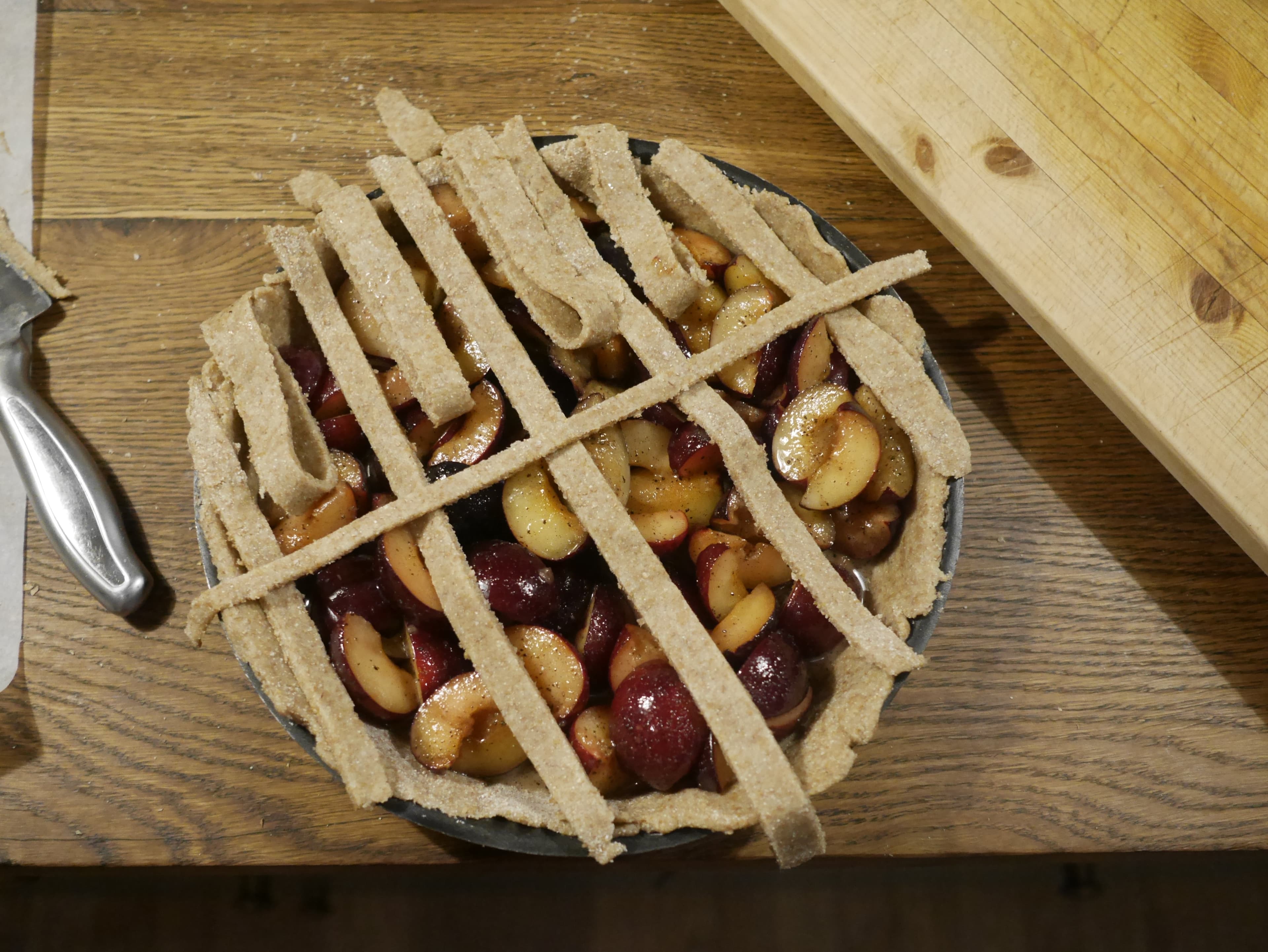 A dough lattice being made on the top of an uncooked plum pie.