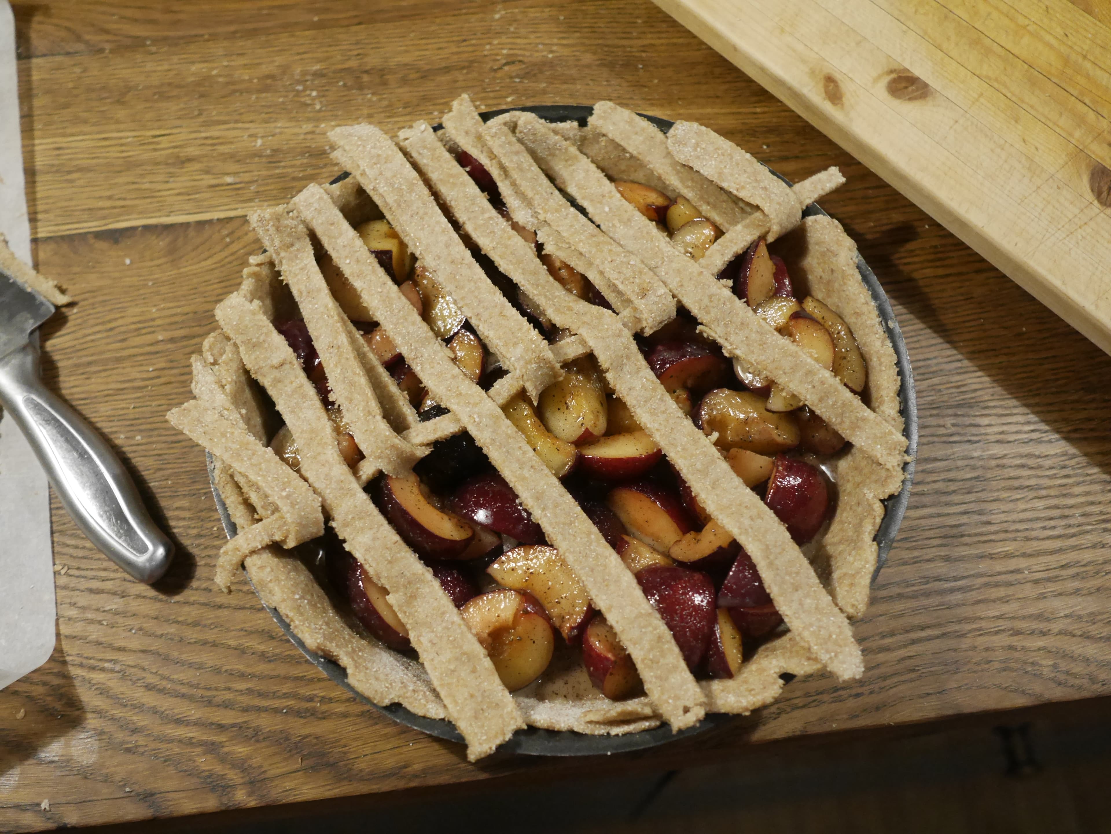 A dough lattice being made on the top of an uncooked plum pie.