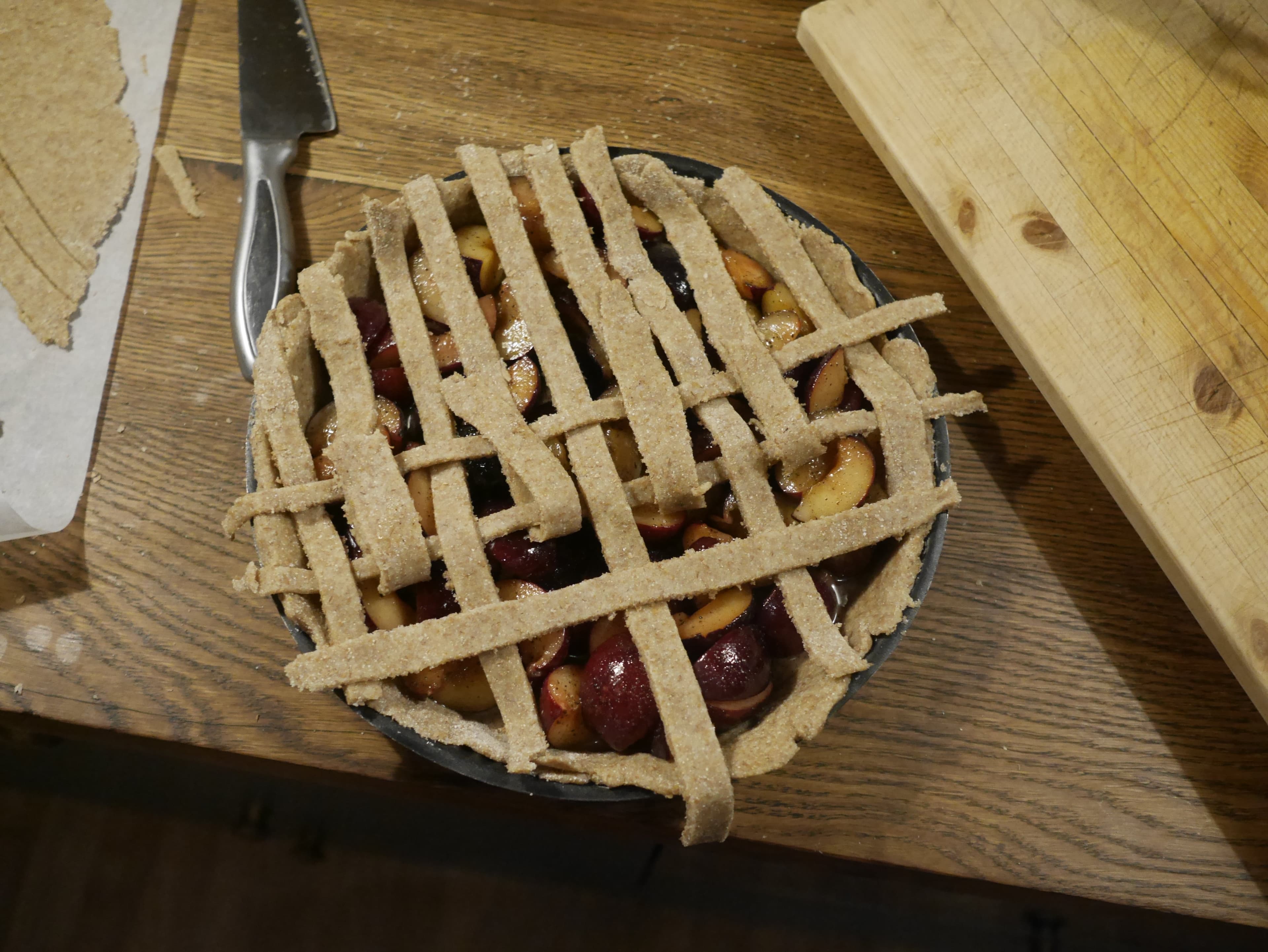 A dough lattice being made on the top of an uncooked plum pie.