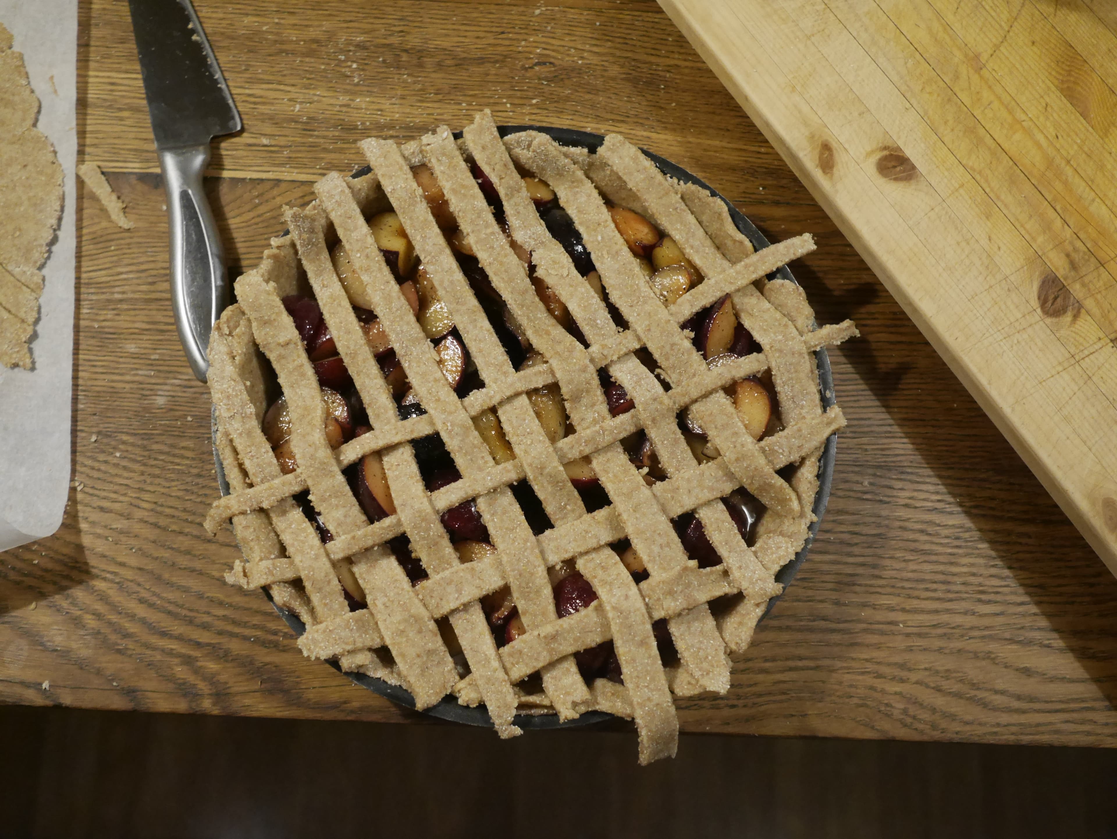 A dough lattice being made on the top of an uncooked plum pie.