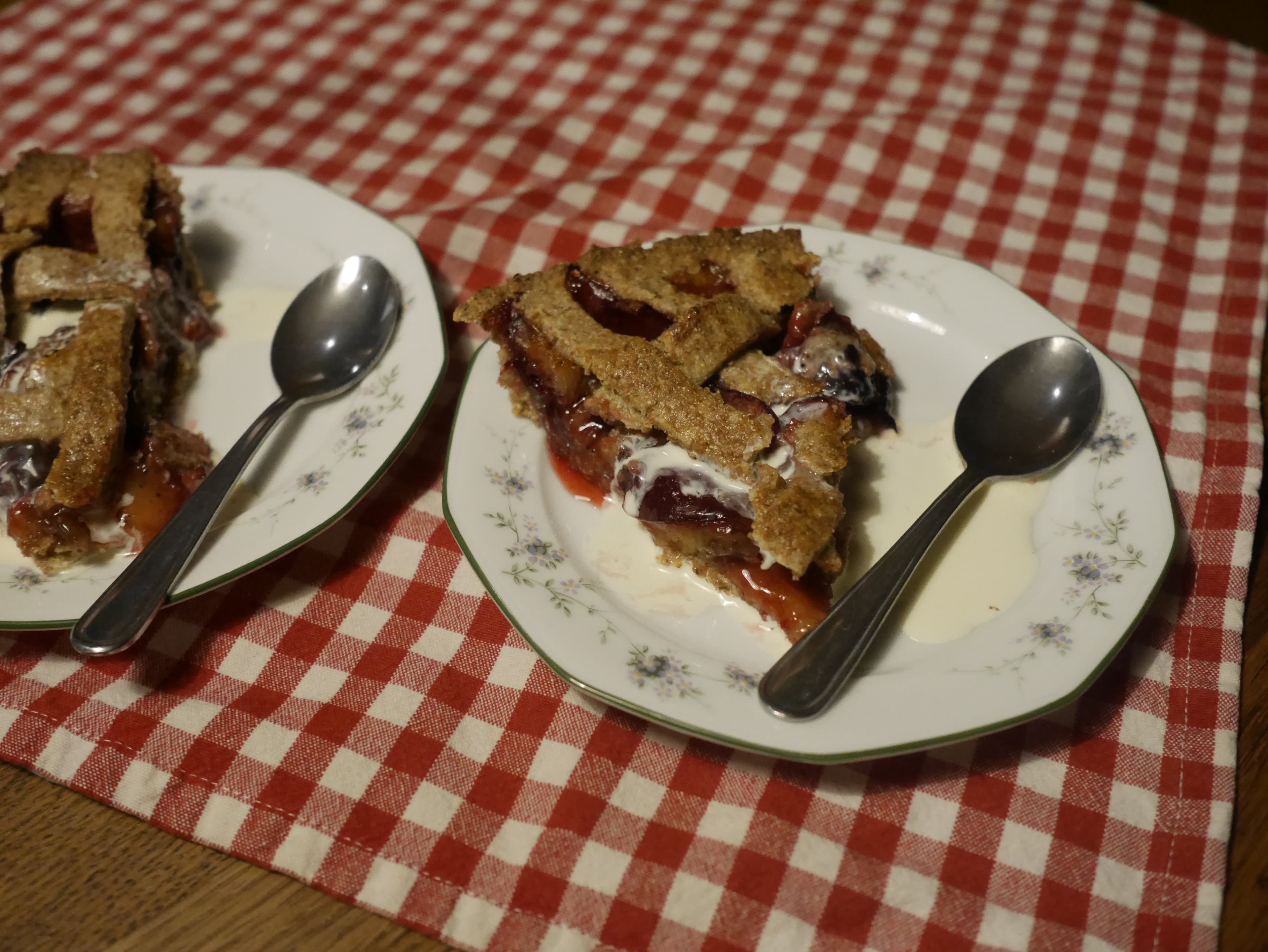 Pieces of plum pie served with cream on a plate.