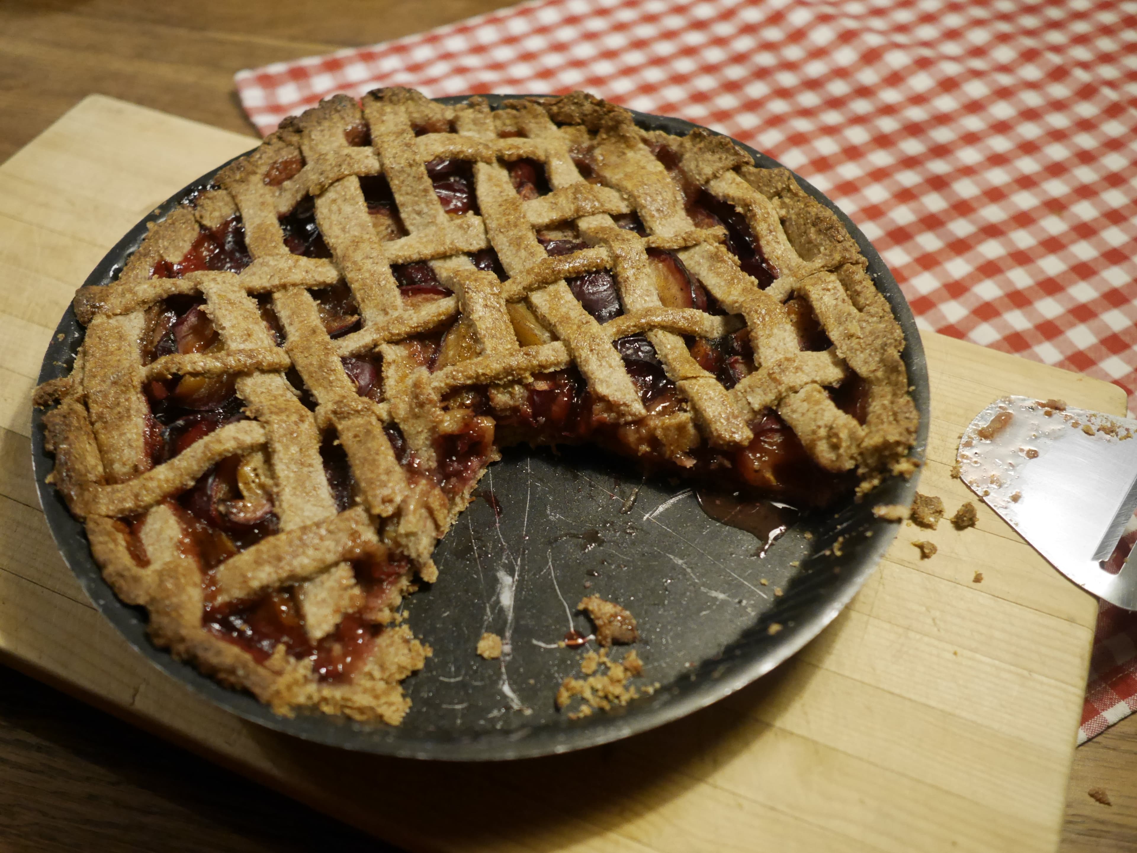 A plum pie in a dish with a few wedges taken from it.