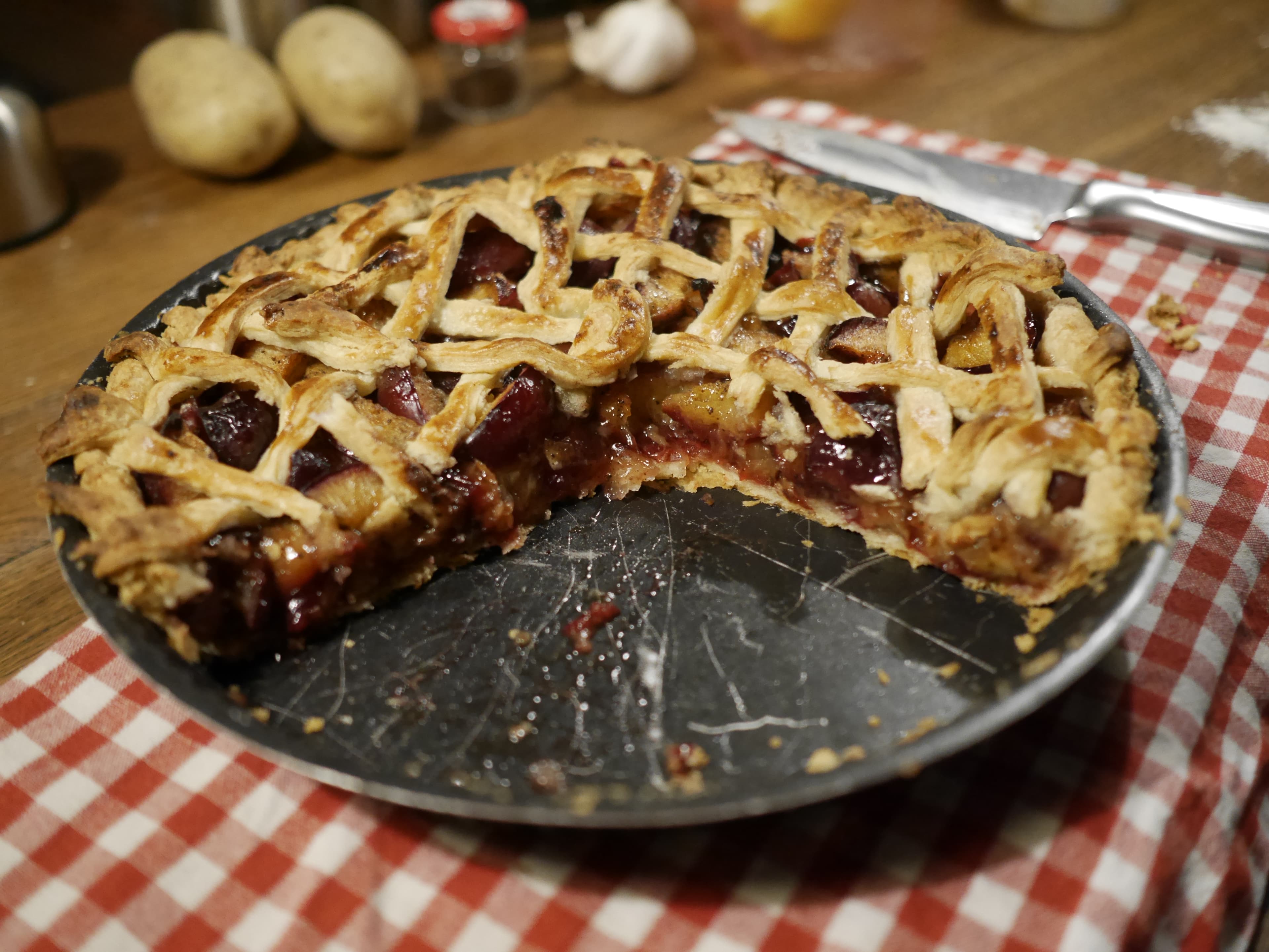 A plum pie in a dish with a few wedges taken from it.